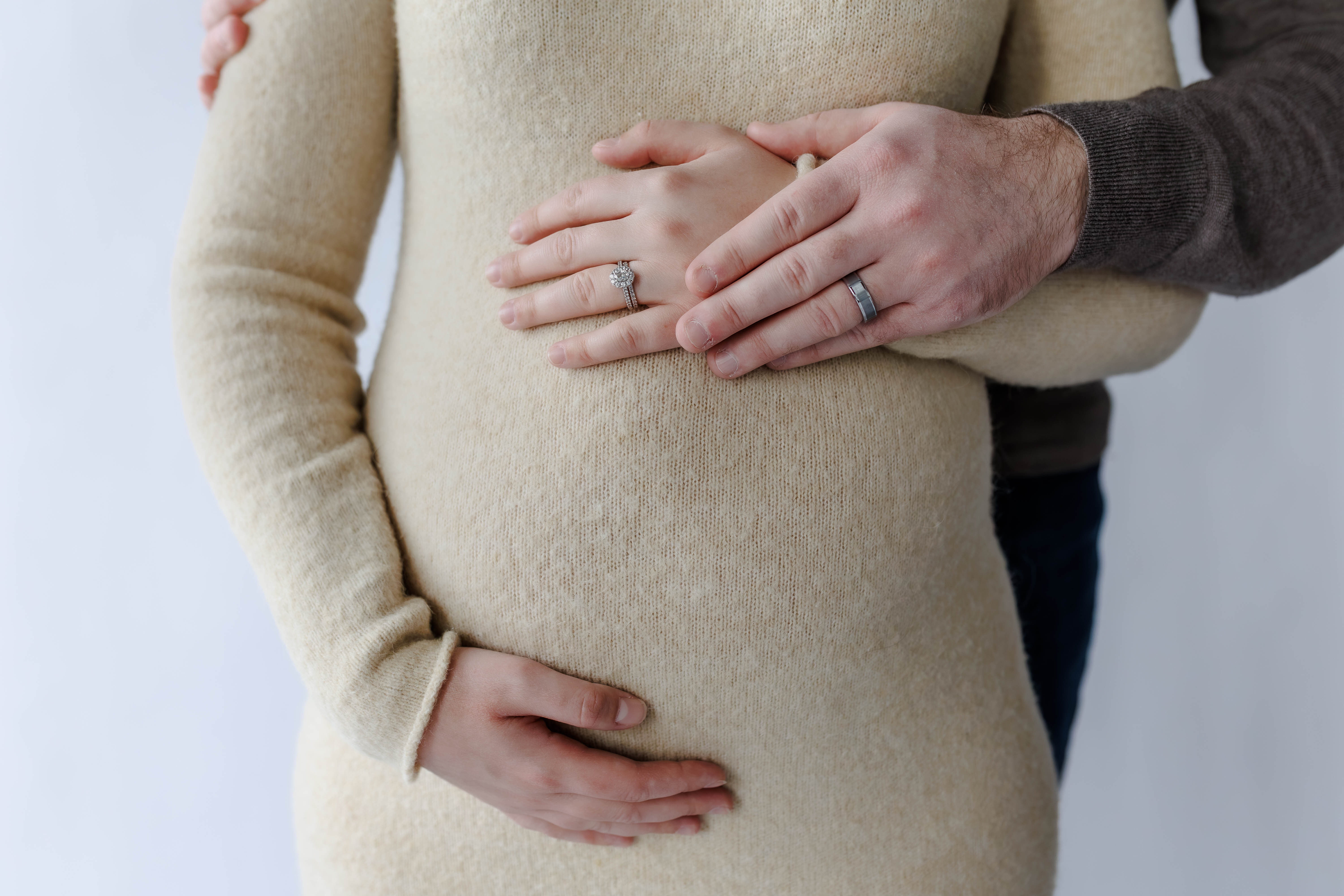 Maternity couple detail: bride and groom hands on belly showing engagement and wedding rings
