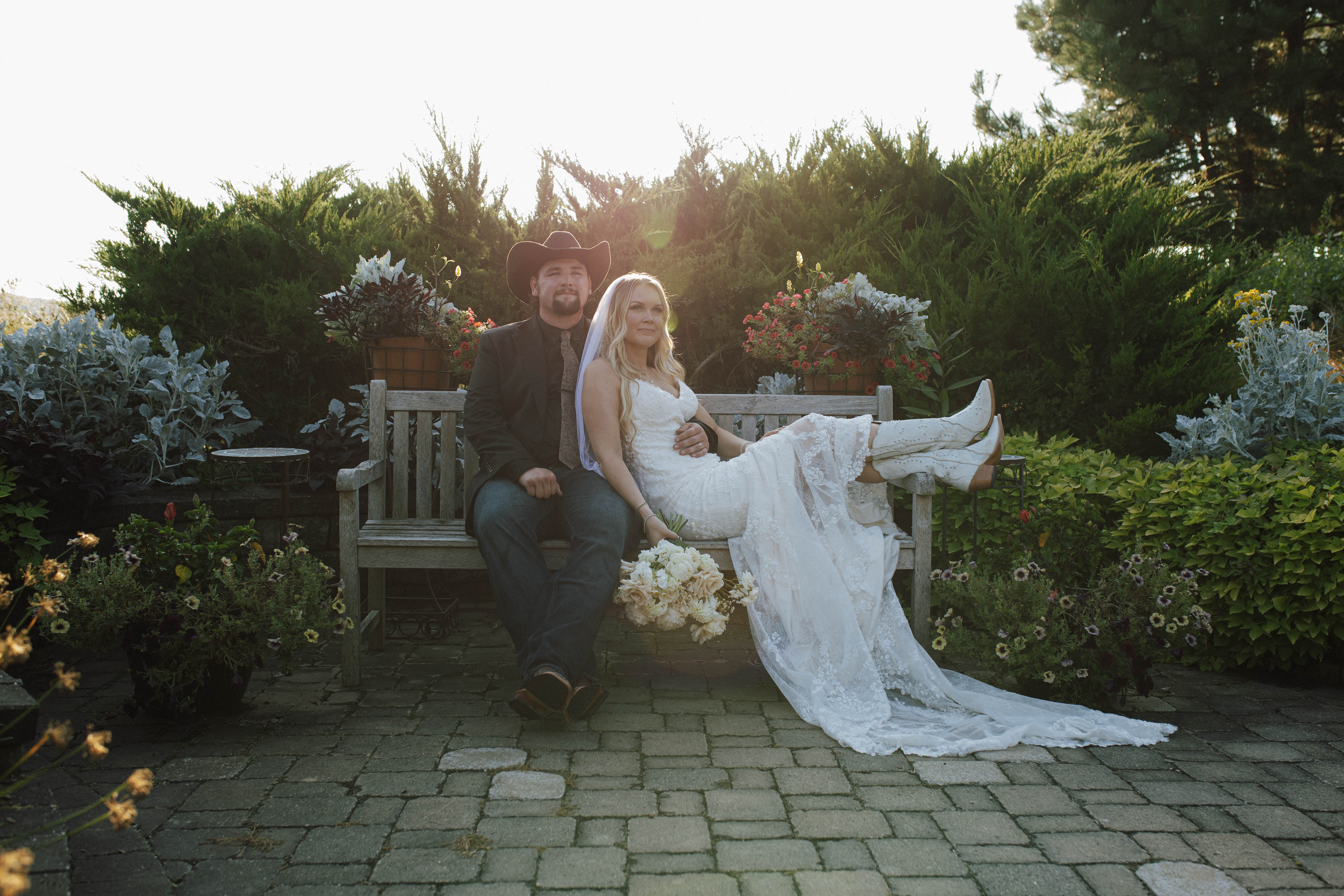 Wisconsin wedding photographer - couple on garden bench at sunset with bride showing white cowboy boots and stunning backlight