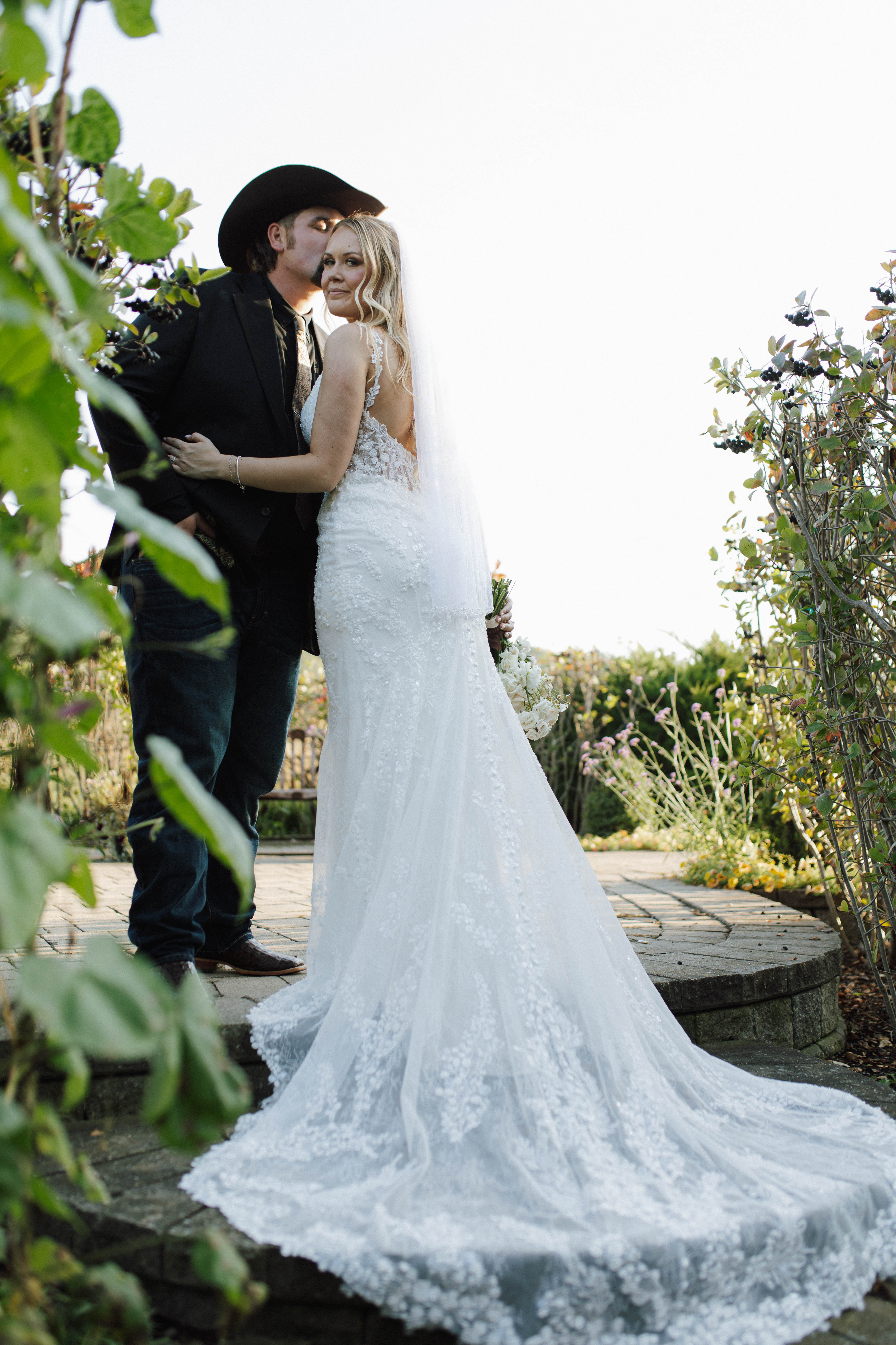Wisconsin wedding photographer - romantic country wedding couple with cowboy hat and lace dress in garden setting with trailing veil