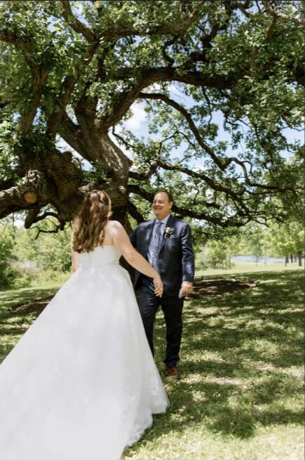 Bride and groom holding hands during a first look under an oak tree in warm natural light